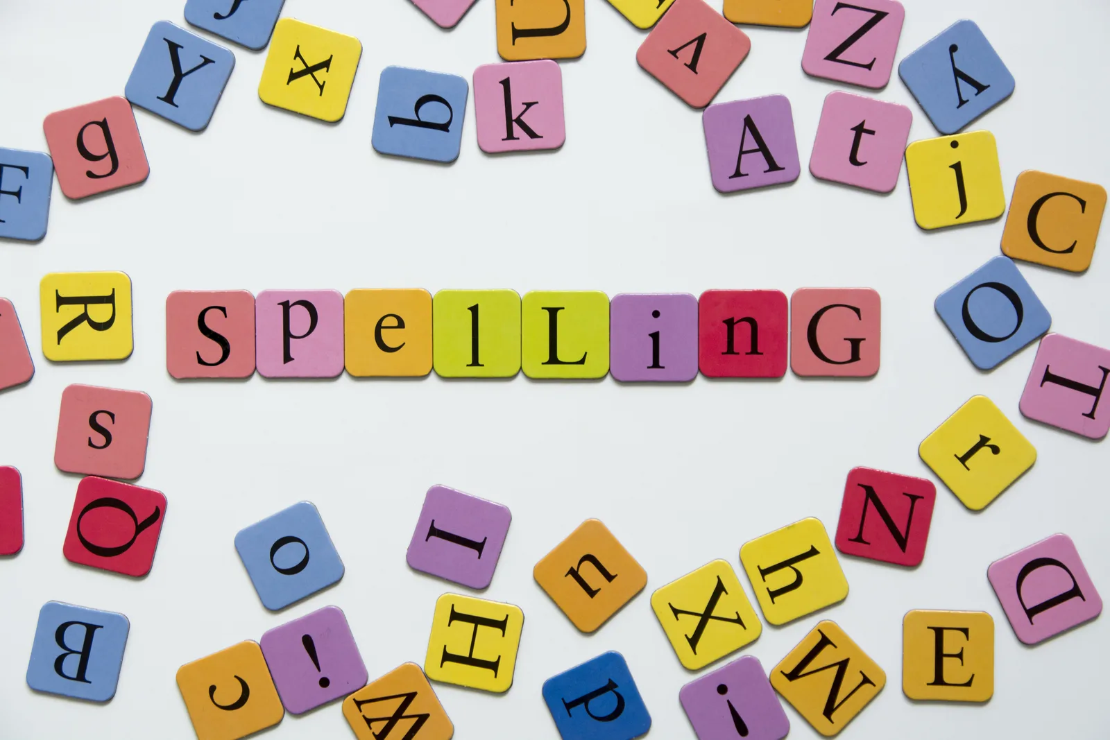 Coloured letter tiles scattered on a table, spelling out the word SPELLING